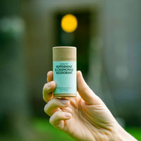 Hand holding a deodorant stick labeled 'Peppermint & Chamomile' against a blurred natural background